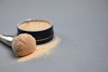 Loose face powder and makeup brush on light grey background, closeup. Space for text