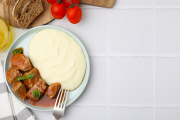 Delicious goulash served with mashed potato on white tiled table, flat lay. Space for text