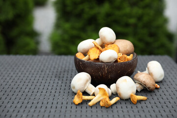 Bowl with different fresh mushrooms on grey rattan table outdoors. Space for text