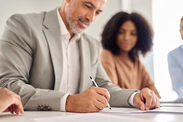 Obraz premium Old senior businessman investor wearing suit signing business legal document. Male bank client writing signature on sales contact making successful investment deal. Focus on hand holding pen. Close up