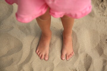 Little girl standing on sandy beach, closeup