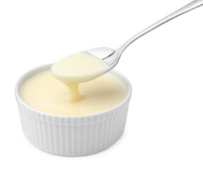 Condensed milk flowing down from spoon into bowl isolated on white