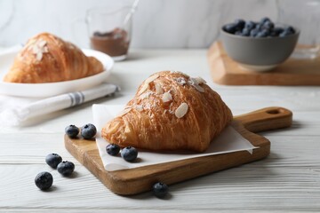 Naklejka premium Delicious croissant with almond flakes and blueberries on white wooden table, closeup