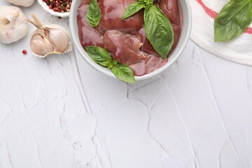 Bowl with raw chicken liver, garlic, peppercorns and basil on white textured table, flat lay. Space for text