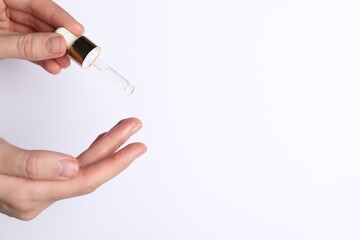 Woman applying cosmetic serum onto fingers on white background, closeup. Space for text