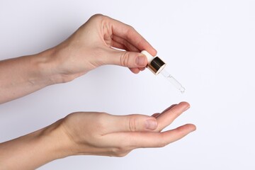 Woman applying cosmetic serum onto fingers on white background, closeup