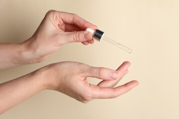 Woman applying cosmetic serum onto finger on beige background, closeup