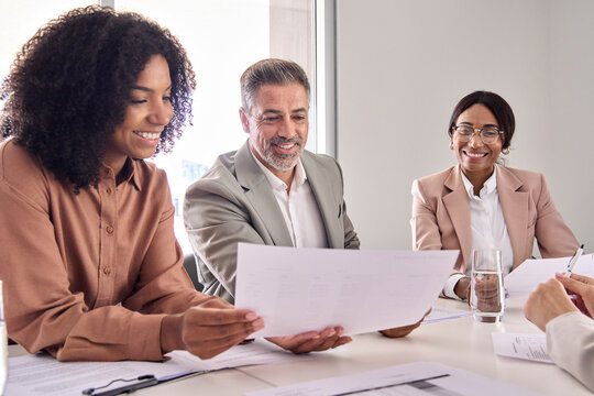 Happy diverse professional executive business people checking document discussing project overview at meeting in boardroom office. Board team colleagues working collaborating at conference table.