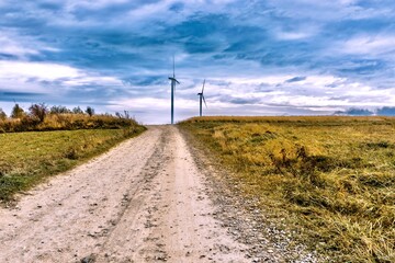 Fototapeta na wymiar Wind turbines on a dirt road in the countryside with stormy sky, Poland.