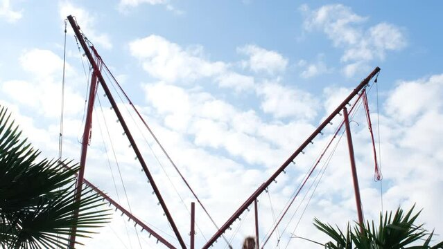 Little girl bouncing on a bungee trampoline in city park in tropics, slow motion. Child high up with safety ropes