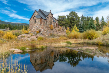Fototapeta premium Saiint Malo Church near Estes Park and Rocky Mountain National Park, Colorado during Fall 2023. Beautiful pond, blue sky, clouds, aspen trees. Catholic church.