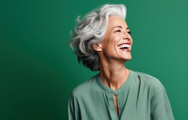 Graceful mature woman with silver hair, exuding joy and elegance against a vibrant green backdrop. Ideal for mature beauty campaigns and age-positive advertisements.