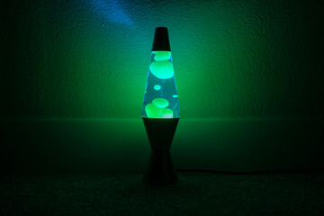 Green and blue lava lamp stands near a white wall in the darkness