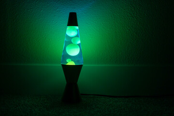 Green and blue lava lamp stands near a white wall in the darkness