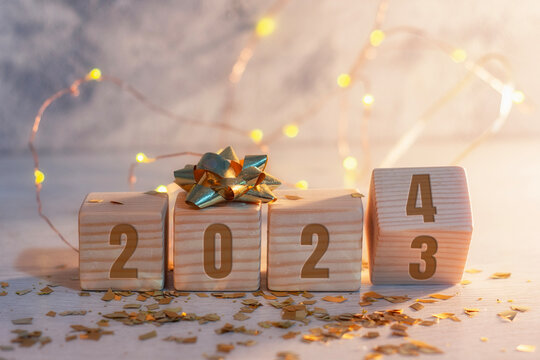 New Year holiday background. Inscription on wooden cubes of the number 2023 and 2024 with bright glowing lights.