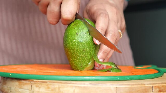 women hand cutting slice of avocado with knife, 