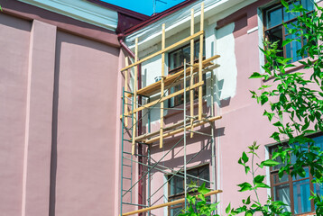 Scaffolding for the work of builders during the repair of the facade of an old building. Painting the building with scaffolding. Facade cladding works during the renovation of the house.