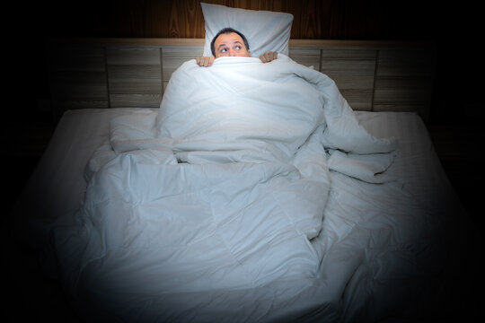 Frightened man in bed hiding under the covers