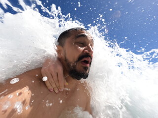 Man Under Tidal Surge: A man is seen experiencing an powerful ocean wave washing over, capturing a...