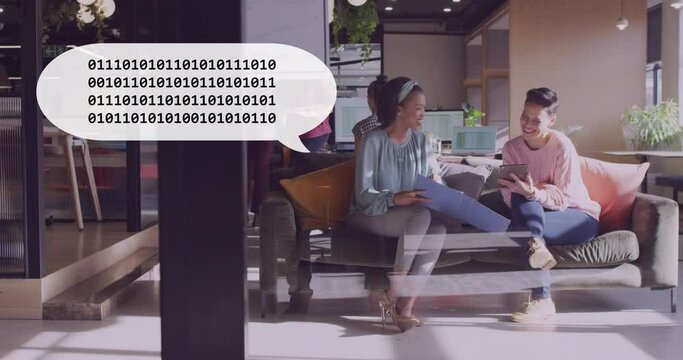 Animation of binary coding on a speech bubble against two diverse women discussing at office