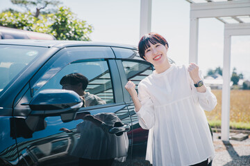 車の前でガッツポーズする女性　A woman posing in front of a car - obrazy, fototapety, plakaty