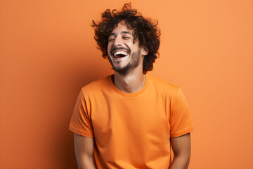 Fototapeta na wymiar Young man, donned in an orange t-shirt, exuberantly laughs against an isolated orange backdrop