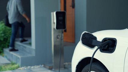 A man unplugs the electric vehicle's charger at his residence. Concept of the use of electric...