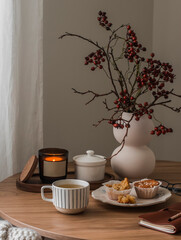 Cup of tea, muffins, cranberry branches in a vase, a notebook, a burning candle on a round wooden...
