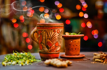 Artesanal tea in a rustic cup and filter with bokeh lights at background