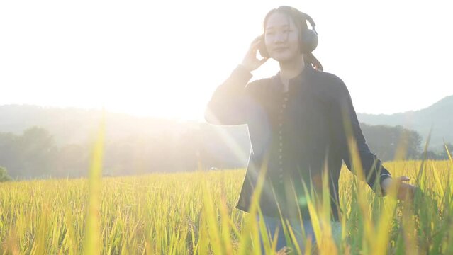 Half length profile portrait of young asian caucasian woman listening music with headphones in rice field at sunset