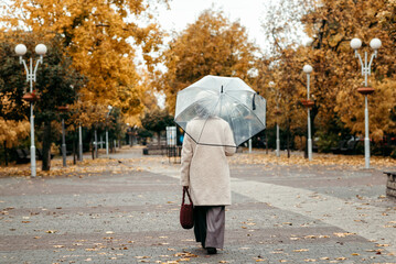 An elderly woman with an umbrella walks along an autumn street