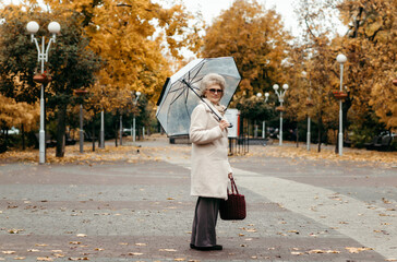 An elderly woman with an umbrella walks along an autumn street