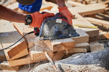 Carpenter using circular saw for cutting wooden plank. Close up of man worker building wooden frame...