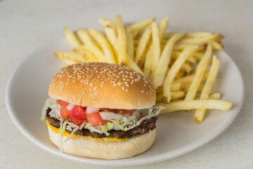 Hamburger with meat, vegetables and fries on a table