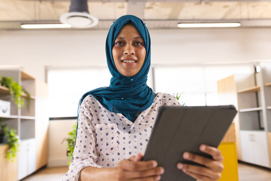 Portrait of happy biracial casual businesswoman with hijab having video call in creative office