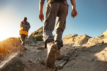 Two young hikers walk with backpacks in mountains at sunset. Close up photo of legs