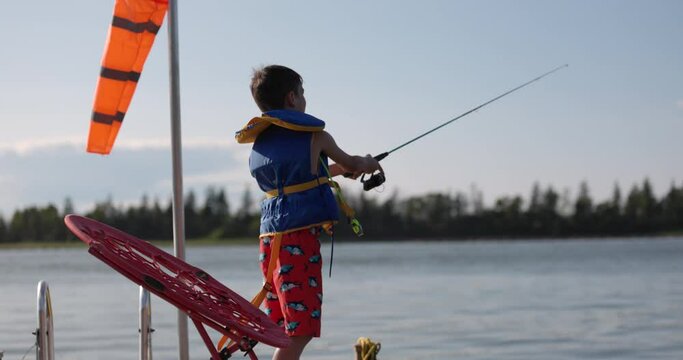 Young boy casts fishing line from cottage dock in summer - summer vacation fun