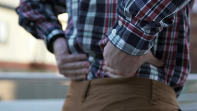 A man feels a sharp pain in his lower back and massages his back during a break at work. Sports and injury concept.