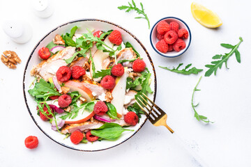 Fresh salad with raspberries, grilled chicken, pears, cheese, onion, walnuts, spinach and arugula, white table background, top view