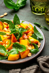 Spicy gourmet salad with sweet peach, hot jalapeno peppers, salted peanuts and green basil, green table background, top view