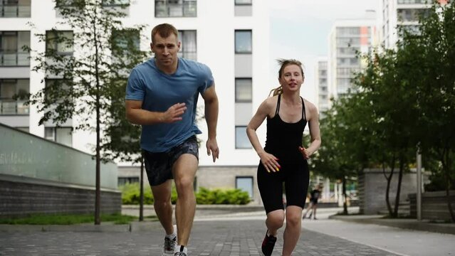 Sprinters start running against the background of residential buildings. Slow motion. A girl and a guy are jogging near the house.
