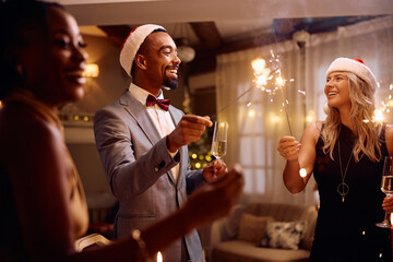 Cheerful friends having fun with sparklers while celebrating Christmas at home.