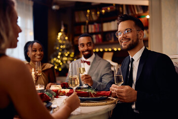 Happy man enjoys in conversation and dinner with his friends at dining table on New Year's eve.