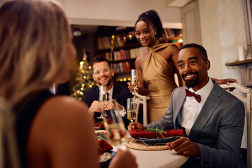 Happy black man talks to his friends during Christmas dinner party.