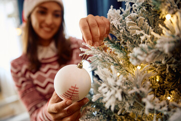 Close up of woman decorating Christmas tree at home. - obrazy, fototapety, plakaty