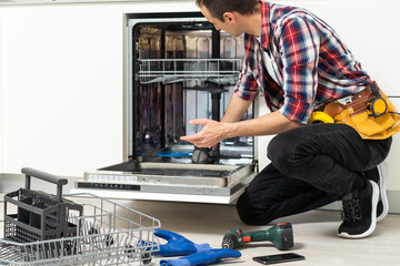 Man repairing a dishwasher with tools - obrazy, fototapety, plakaty