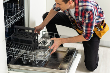 man repairing dishwasher. Male hand with screwdriver installs kitchen appliances, close up