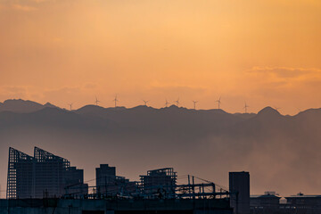 Windmills on the tops of mountains at sunset, above the silhouettes of urban buildings