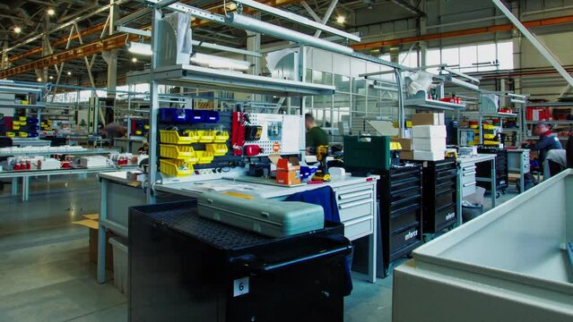 Employees work at tables assembling devices from details taken from boxes on shop floor. Staff members use special equipment in process time lapse