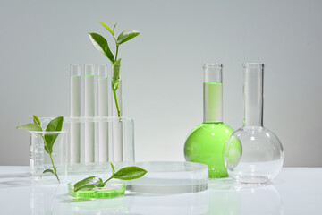 On a white background, some green tea leaves, a few test tubes containing clear liquid, a beaker holding green liquid extracted from green tea. Mockup for pharmaceutical or cosmetic advertising. - obrazy, fototapety, plakaty